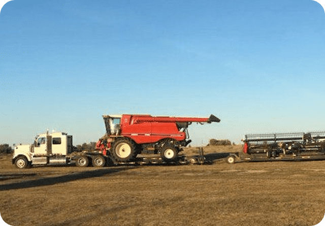 A large red combine harvester on a flatbed trailer in a rural area.