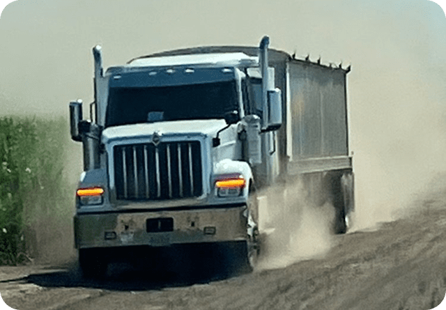 A large dump truck kicks up dust while driving on a dirt road.