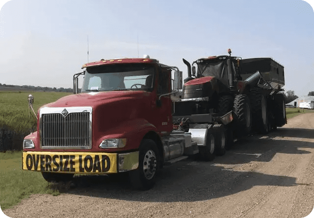 A semi-truck hauling a large black tractor on a trailer labeled 'Oversize Load'.