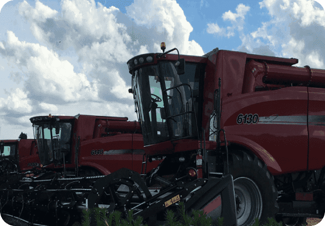 Two red agricultural machines under a partly cloudy sky.